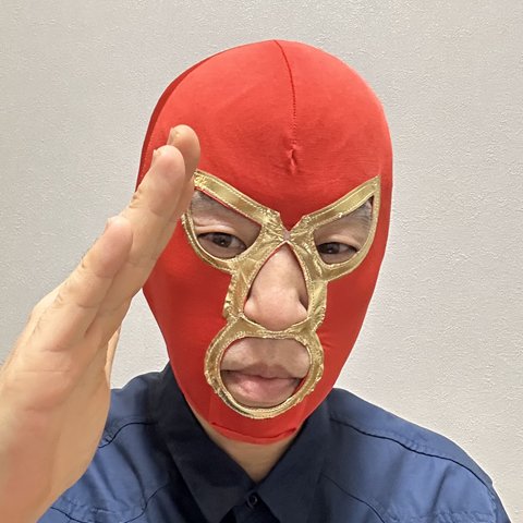 ケンゴのプロフィール写真。赤いレスラーのマスクをかぶり、片手を顔の横に上げている